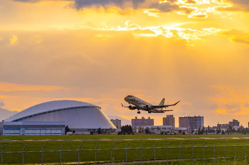 丘珠空港を離陸するゴールドの9号機と背景の「つどーむ」
